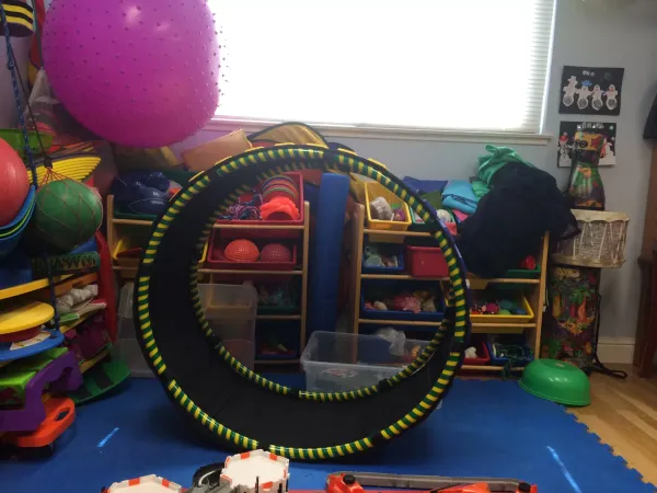 A striped tunnel hoop in front of shelves of colorful therapy toys